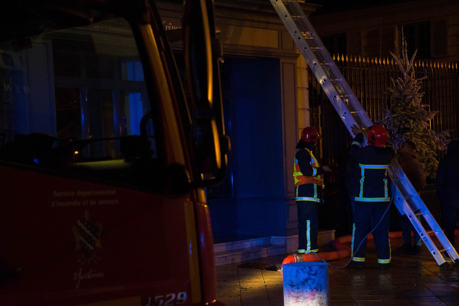 Deux sapeurs-pompiers manœuvrent une échelle de nuit, éclairés par les gyrophares de leur engin
